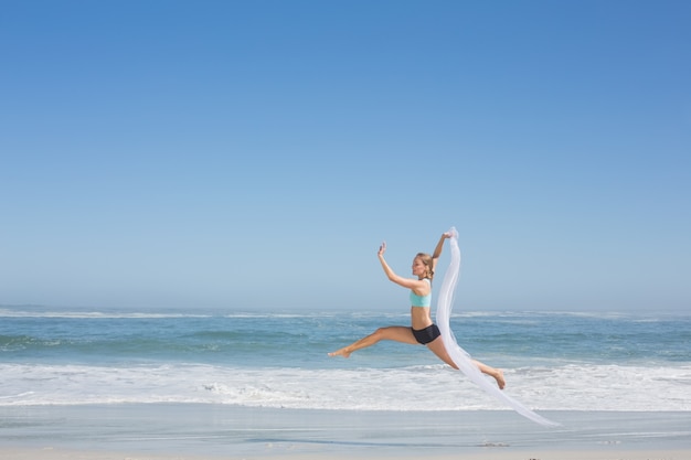 Geeignete Frau, die würdevoll auf den Strand mit Schal springt