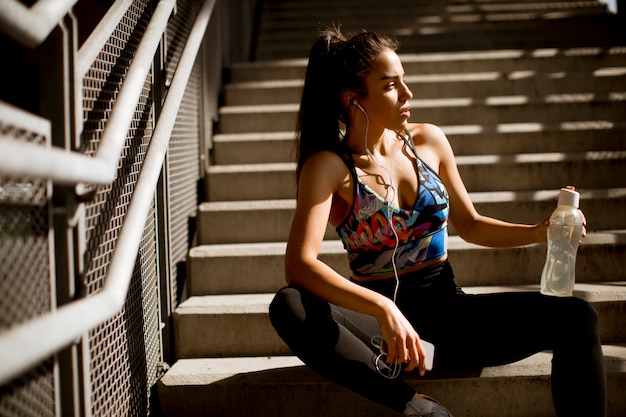 Foto geeignete sportliche frau der junge, die stillsteht und hören musik am handy nach der ausbildung im freien auf treppe in der städtischen umwelt