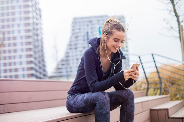 Geeignete sportliche Frau der Junge, die stillsteht und hören Sie Musik am Handy nach der Ausbildung