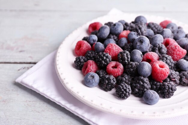 Geeiste Beeren auf Platte auf farbigem Holzhintergrund