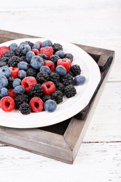 Geeiste Beeren auf Platte auf farbigem Holzhintergrund