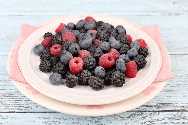 Geeiste Beeren auf Platte auf farbigem Holzhintergrund