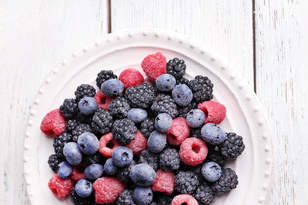 Geeiste Beeren auf Platte auf farbigem Holzhintergrund