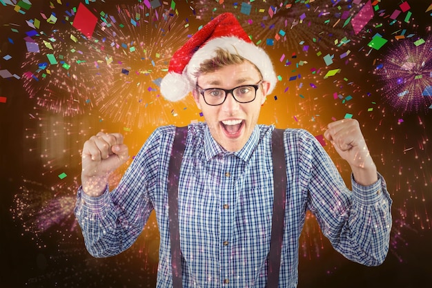 Geekiger Hipster mit Weihnachtsmütze vor buntem Feuerwerk, das auf schwarzem Hintergrund explodiert