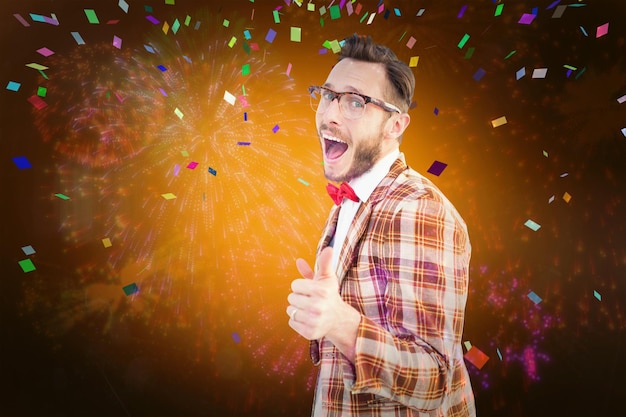 Geeky hipster apontando para a câmera contra fogos de artifício coloridos explodindo em fundo preto