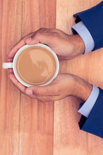 Geerntete Hände des Geschäftsmannes Kaffeetasse auf hölzernem Schreibtisch im kreativen Büro halten