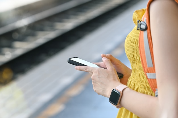 Geerntete Schussfrau, die intelligentes Telefon verwendet und auf Bahnstation wartet.