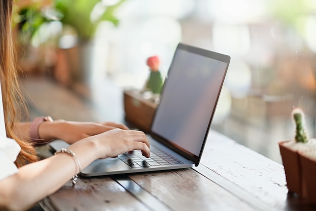 Geerntete Schussgeschäftsfrauhand, die an einem Laptop am Schreibtisch im Café arbeitet.