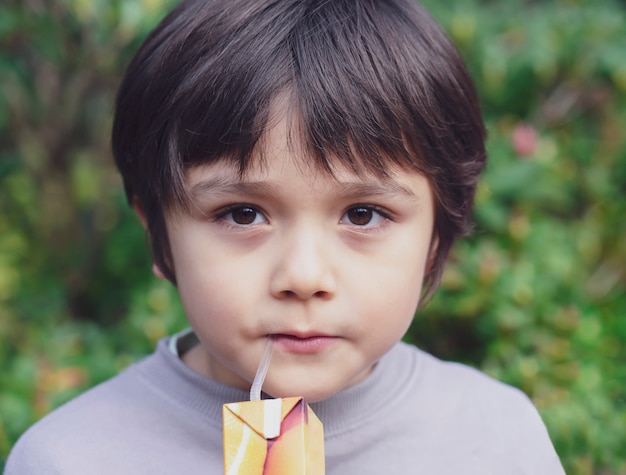 Geernteter Schuss des Kindes stehend im Garten etwas Saft trinkend, gesunder Kinderjunge, der frischen Saft trinkt.