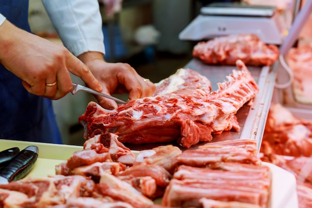 Geerntetes Bild des männlichen Metzgers rohes Fleisch mit Messer am Gegengeschäft schneiden