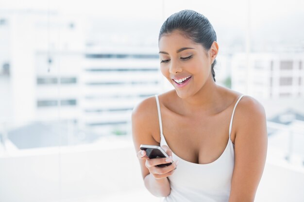 Gefälliger getonter Brunette, der Handy hält