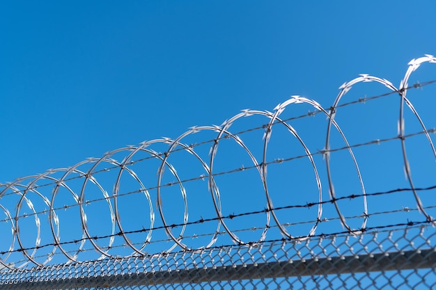 Gefängnismauer. hochgeschützte Gefängnismauer mit Stacheldrahtzaun. Gitterzaun aus Stahl. aufgewickelter Stacheldraht mit seinen scharfen Stahlwiderhaken auf dem Maschendrahtzaun. Gewährleistung von Sicherheit und Geborgenheit.