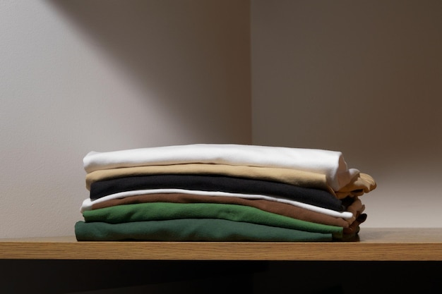 Gefaltete T-Shirts in den Farben Weiß, Beige und Grün auf einem Holzregal eines Schranks. Das Konzept der kompakten Aufbewahrung von Kleidung zum Wechseln oder Aufrüsten der Garderobe