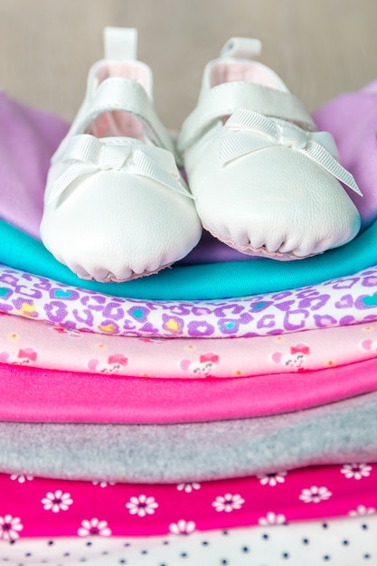 Gefalteter rosa und weißer Bodysuit mit Schuhen auf ihm auf grauem hölzernem Hintergrund.