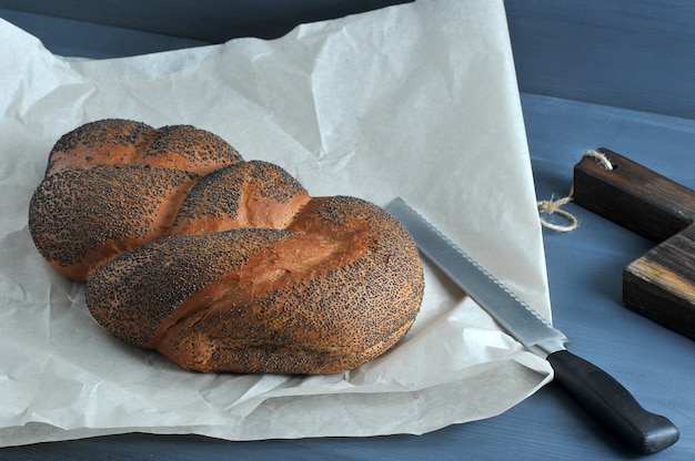 Geflochtenes Brot mit Mohn auf braunem Papier mit einem Brotmesser