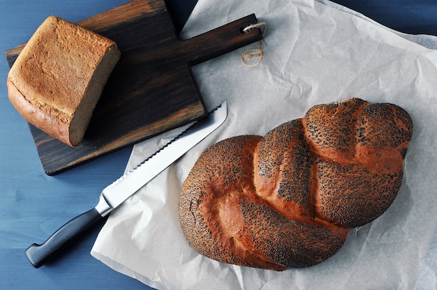 Geflochtenes Brot mit Mohn auf braunem Papier mit einem Messer für das Brot und die Hälfte des Brotes