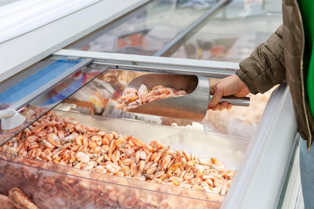 Gefrorene Garnelen im Kühlschrank im Supermarkt Die Hand der Käuferin nimmt eine Eisenschaufel auf Nahaufnahme Gesunde Ernährung und Ernährung