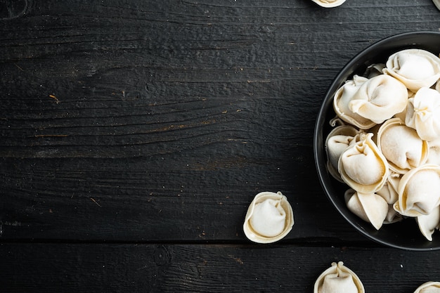 Gefrorene Knödel Tortellini und Ravioli in schwarzer Schüssel, auf schwarzem Holztisch Hintergrund, Draufsicht flach legen,