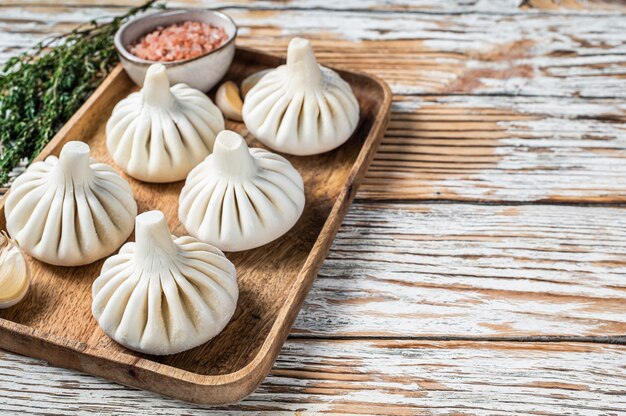 Gefrorene rohe Teigtaschen Khinkali mit Rind- und Lammfleisch auf Holztablett mit Kräutern. Weißer hölzerner Hintergrund. Ansicht von oben. Platz kopieren.