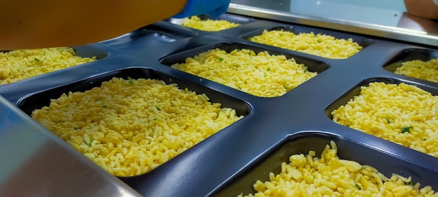 Gefrorener gebratener Reis mit Ei in Plastikschale wartet auf Top-Siegel-Etikett mit Thermoformmaschine in Lebensmittelfabrik. Tiefkühlkostindustrie. Fertiggerichtsverfahren in der Herstellung. Lebensmittelverpackungsindustrie.