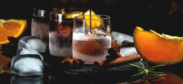 Gefrorener Kräuterlikör in kleinem Glas Schnapsglas Kräuterlikör mit Zimt und Orangen auf dunklem Hintergrund