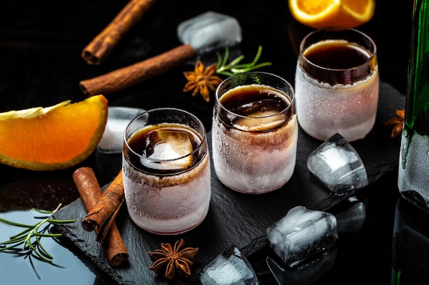 Gefrorener Kräuterlikör in kleinem Glas Schnapsglas Kräuterlikör mit Zimt und Orangen auf dunklem Hintergrund