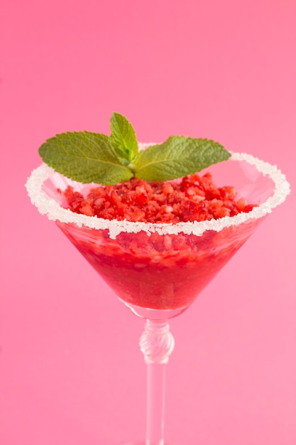 Gefrorener Saft mit Erdbeere in einem Martini-Glas auf dem rosa Hintergrund. Lage vertikal. Nahansicht.