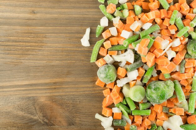 Gefrorenes gemischtes Gemüse auf Holztisch. Rohe gehackte Karotten, Blumenkohl, Zwiebeln, grüne Bohnen und Rosenkohl