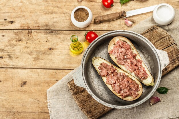 Gefüllte Auberginen zum Backen mit Hackfleisch, Gemüse und Gewürzen. Hölzerner Hintergrund, Küchengerät, rustikaler Stil, Draufsicht