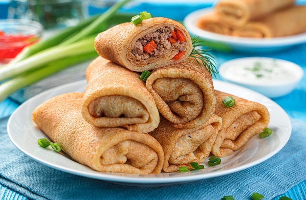 Gefüllte Pfannkuchen mit Fleisch und Karotten auf blauem Hintergrund mit Sauerrahmkräutern und Kaviar