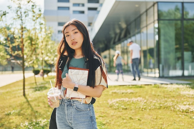 Gegen modernes Gebäude stehend Junge asiatische Frau ist tagsüber im Freien