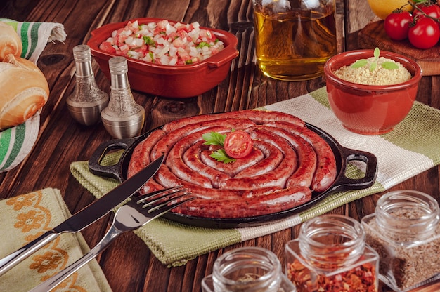 Gegrillte brasilianische Wurst auf Eisenplatte mit Brot, Salat, Farofa und Gewürzen