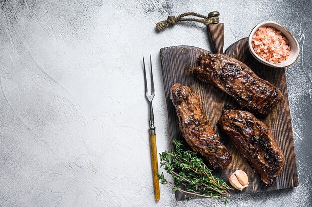 Gegrillte Brisketsteaks in Bbq-Sauce auf einem Holzbrett auf Weiß. Draufsicht.