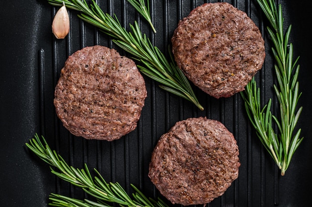 Gegrillte Burger-Fleischpasteten mit Gewürzen auf Grillpfanne Schwarzer Hintergrund Draufsicht