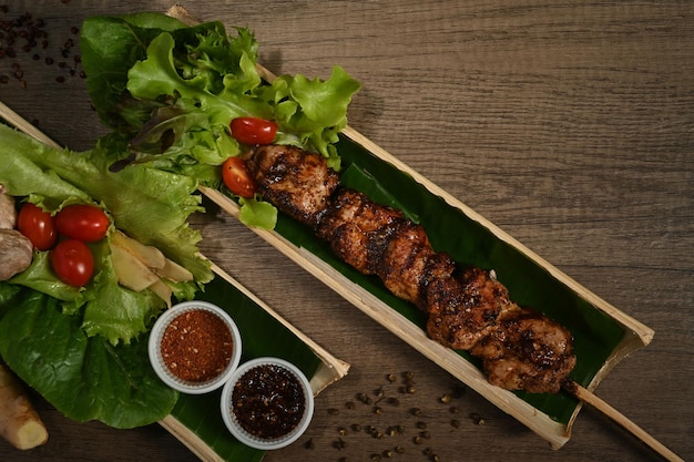 Gegrillte Fleischspieße serviert in einem Bambusfassteller mit Sichuanpfeffer, chinesischen Gewürzen und Gemüse auf einem Holztisch