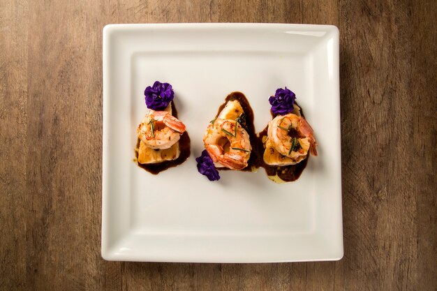 Gegrillte Garnelen mit rohem Nagelfisch auf weißem Teller am Tisch