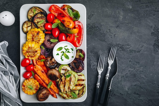 Gegrillte Gemüseplatte mit Zucchini-Pilzen, Auberginen, Karotten, Paprika, Tomaten, Zwiebeln, Mais und Joghurt-Minz-Sauce. Draufsicht