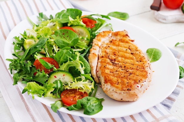 Gegrillte Hähnchenbrust und frischer Gemüsesalat - Tomaten, Gurken und Salatblätter. Hühnchensalat. Gesundes Essen.