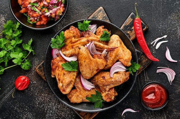 Gegrillte Hähnchenflügel oder gebratener Grill mit Gewürzen und Tomaten-Salsa-Sauce auf einem schwarzen Teller.