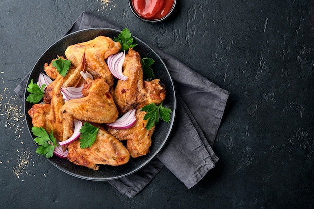 Gegrillte Hähnchenflügel oder gerösteter Grill mit Gewürzen und Tomatensalsasauce auf einem schwarzen Teller. Draufsicht