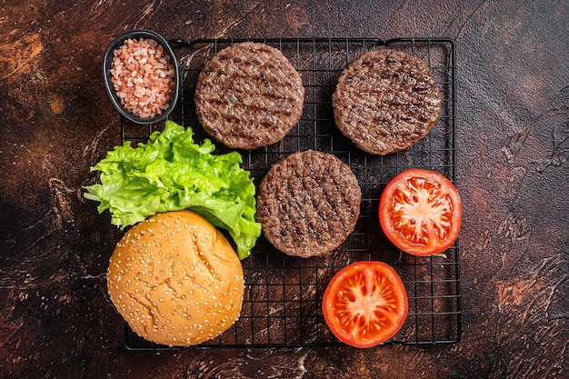 Gegrillte hamburger-pastetchen mit tomaten und gewürzen auf küchentisch dunkler hintergrund ansicht von oben