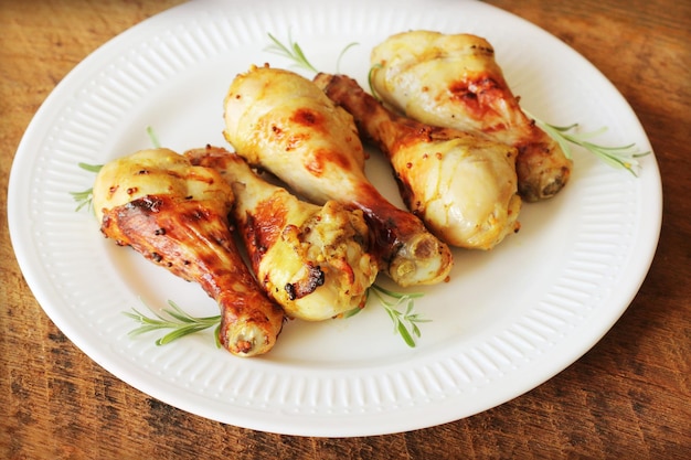 Foto gegrillte hühnerbeine mit senf auf einem holztisch, serviert auf einem weißen teller mit rosmarin bbq-abendessen.