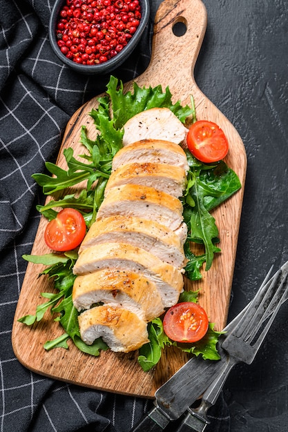 Gegrillte Hühnerbrust. Hähnchenfilet und frischer Gemüsesalat mit Tomaten und Rucola-Blättern. Schwarzer Hintergrund. Draufsicht