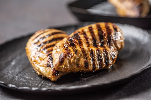 Gegrillte Hühnerbrust in schwarzer Platte auf Küchentisch.