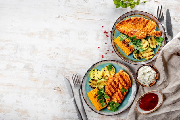 Foto gegrillte hühnerbrust mit mais und zucchini auf einer blauen platte-draufsicht. sommergericht mit gegrilltem huhn und gemüse.