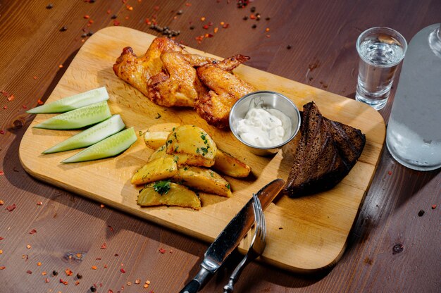 Gegrillte Hühnerflügel vom Grill schließen oben mit Pommes Frites, Soße auf Holzbrett auf einem dunklen Tisch. Fleischnahrungsmittelkonzept. Gebratene Hähnchenschenkel mit Pommes Frites