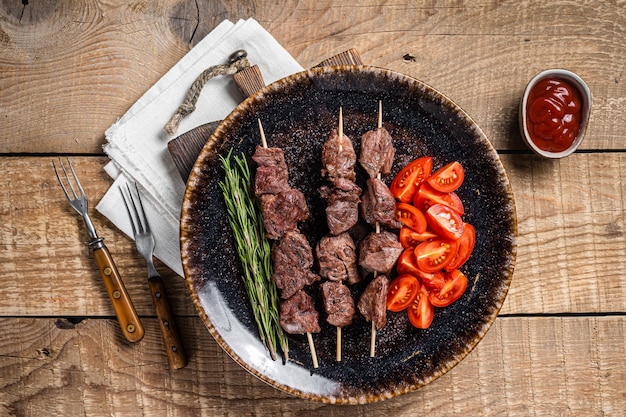 Gegrillte kalbskebab-spieße oder schaschlik in einem teller mit tomaten. hölzerner hintergrund. ansicht von oben.