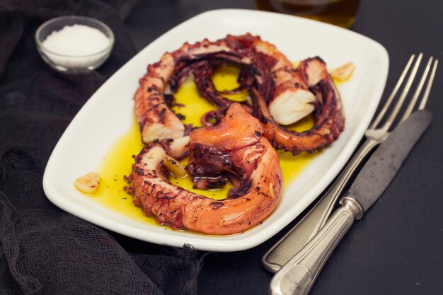 Gegrillte Krake mit Knoblauch auf weißem Teller auf hölzernem Hintergrund