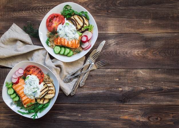 gegrillte Lachsauberginen und Tomaten mit Quinoa und Tzatziki-Sauce auf rustikalem Holzhintergrund