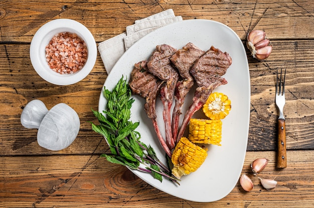 Gegrillte Lammkoteletts Steaks in einem Teller mit Mais und Tomate. hölzerner Hintergrund. Ansicht von oben.